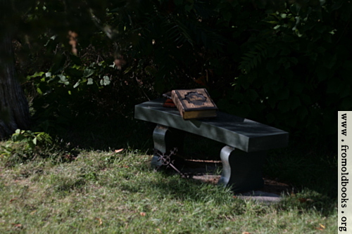 [Picture: Stone bench with books and cross]